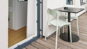 Un patio exterior con una mesa y sillas, una puerta que da a una habitación interior y una ventana con vistas.