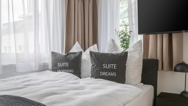 Una habitación de hotel moderna con una cama grande, ropa de cama gris y un televisor de pantalla plana.