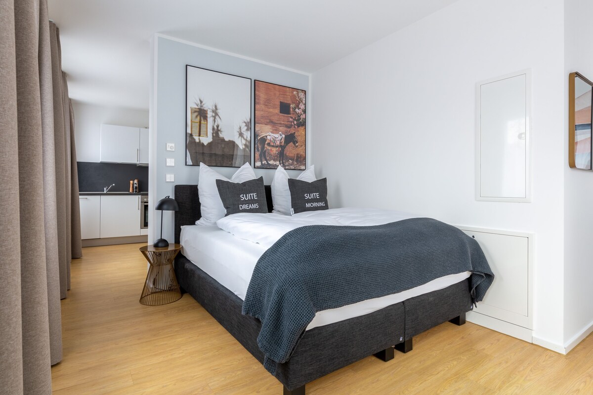 A modern hotel room with a large bed, a small kitchenette, and a view of the city.