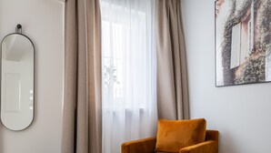 Una habitación con un ventanal grande, una silla, un reposapiés redondo y un espejo montado en la pared.