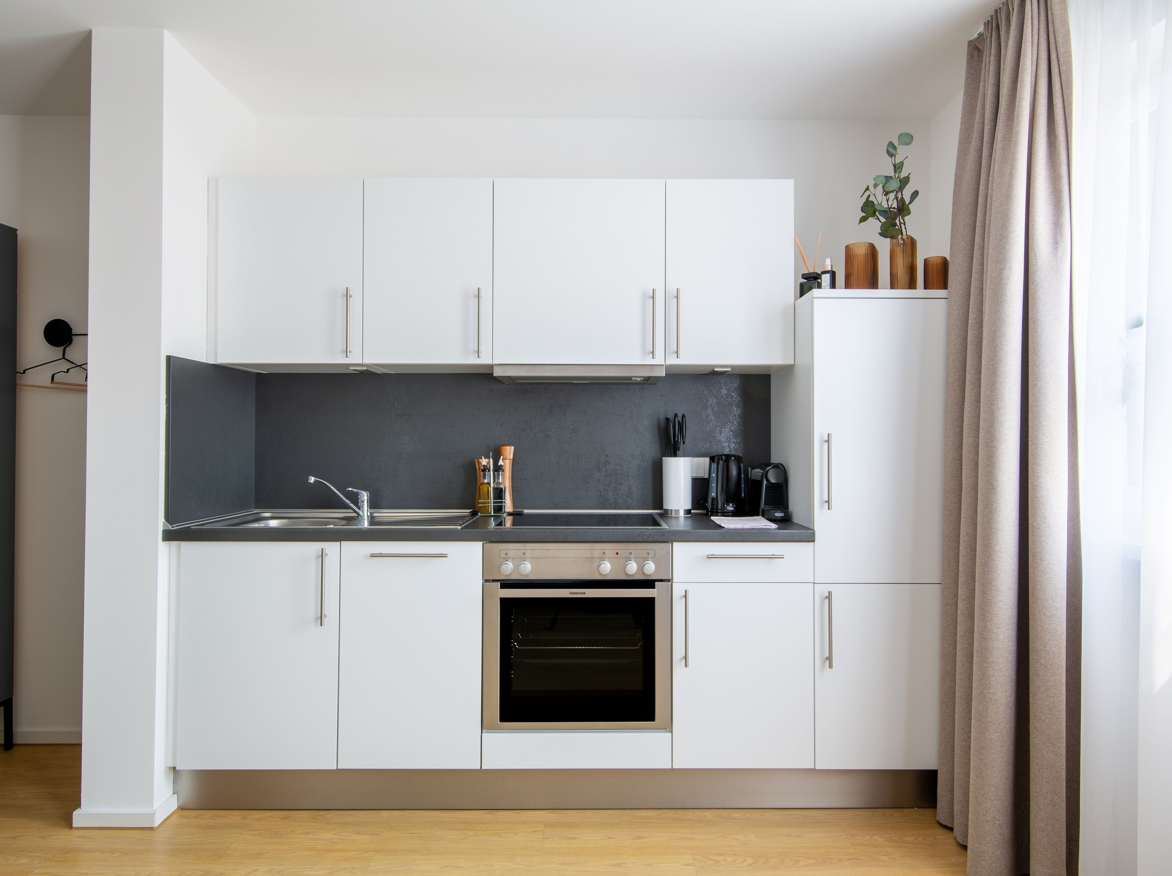 A modern kitchen with white cabinets, a black countertop, and an oven.