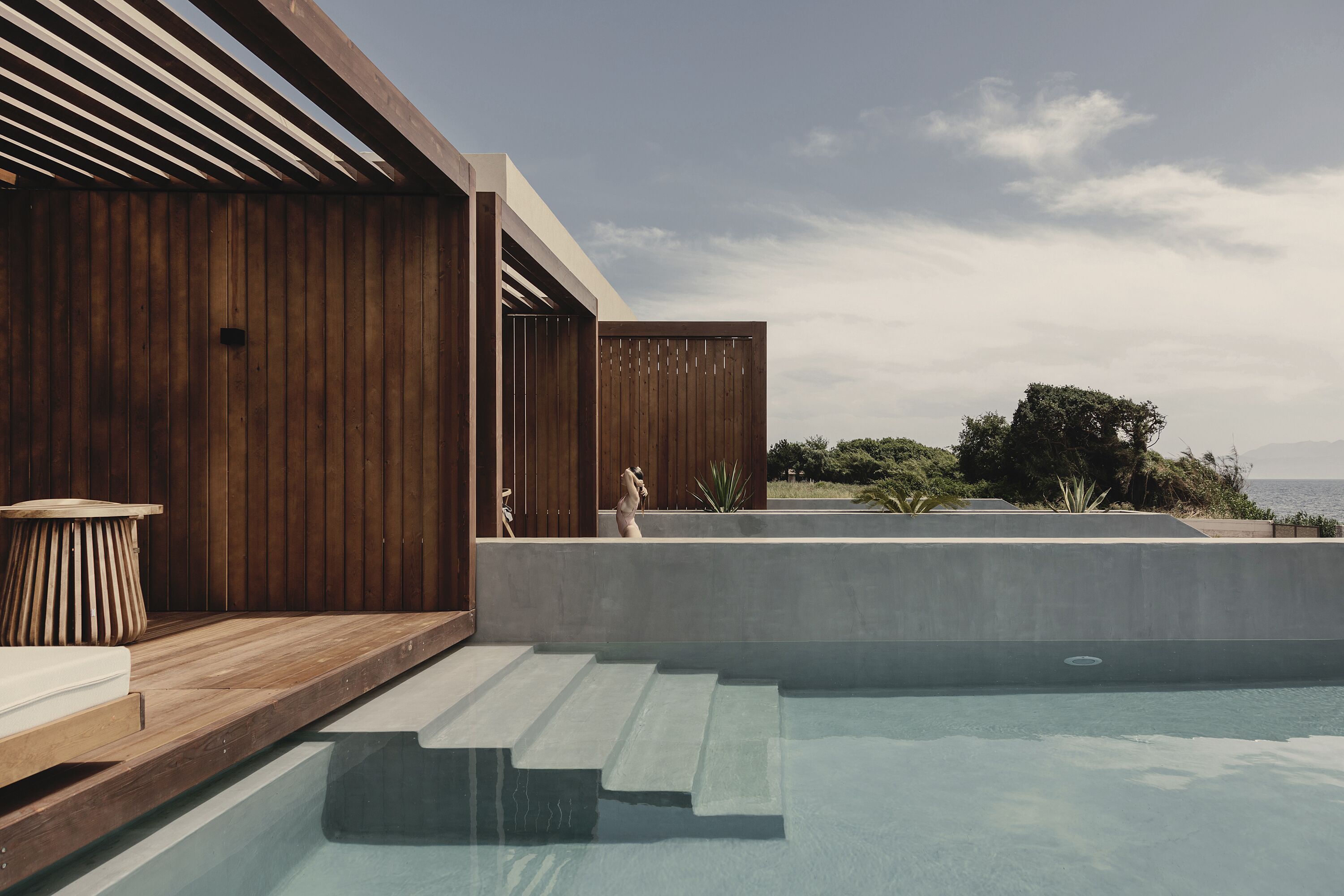 Un espace piscine extérieur moderne, doté d’une terrasse en bois et de marches menant à l’eau, entouré d’une clôture en bois et offrant une vue sur la mer.