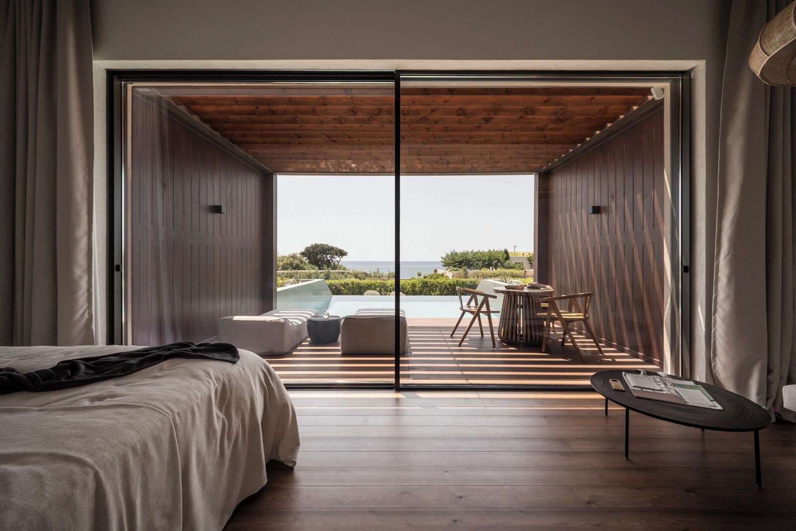 Een moderne slaapkamer met een grote schuifglazen deur die uitkomt op een balkon met een zwembad en buitenmeubels.