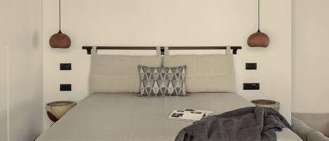 Un dormitorio con techo de madera, una cama con manta gris, almohada gris y una cesta tejida en el suelo.