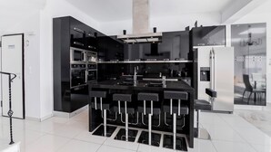 Een moderne keuken met een centraal eiland, zwarte kastjes, roestvrijstalen apparatuur en een bar met krukken.