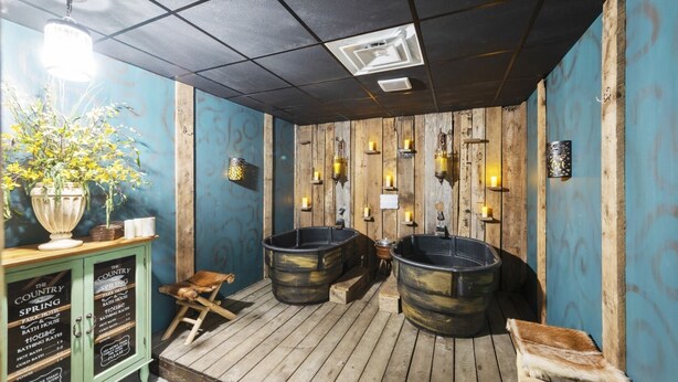 Ein rustikales Badezimmer mit Holzwänden, zwei großen Badewannen, einer Holzbank und einem grünen Schrank mit einem Schild.