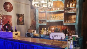 Eine Bar mit Holztresen, einem Schild mit der Aufschrift 'OPEN' und Regalen voller Flaschen und Gläsern.