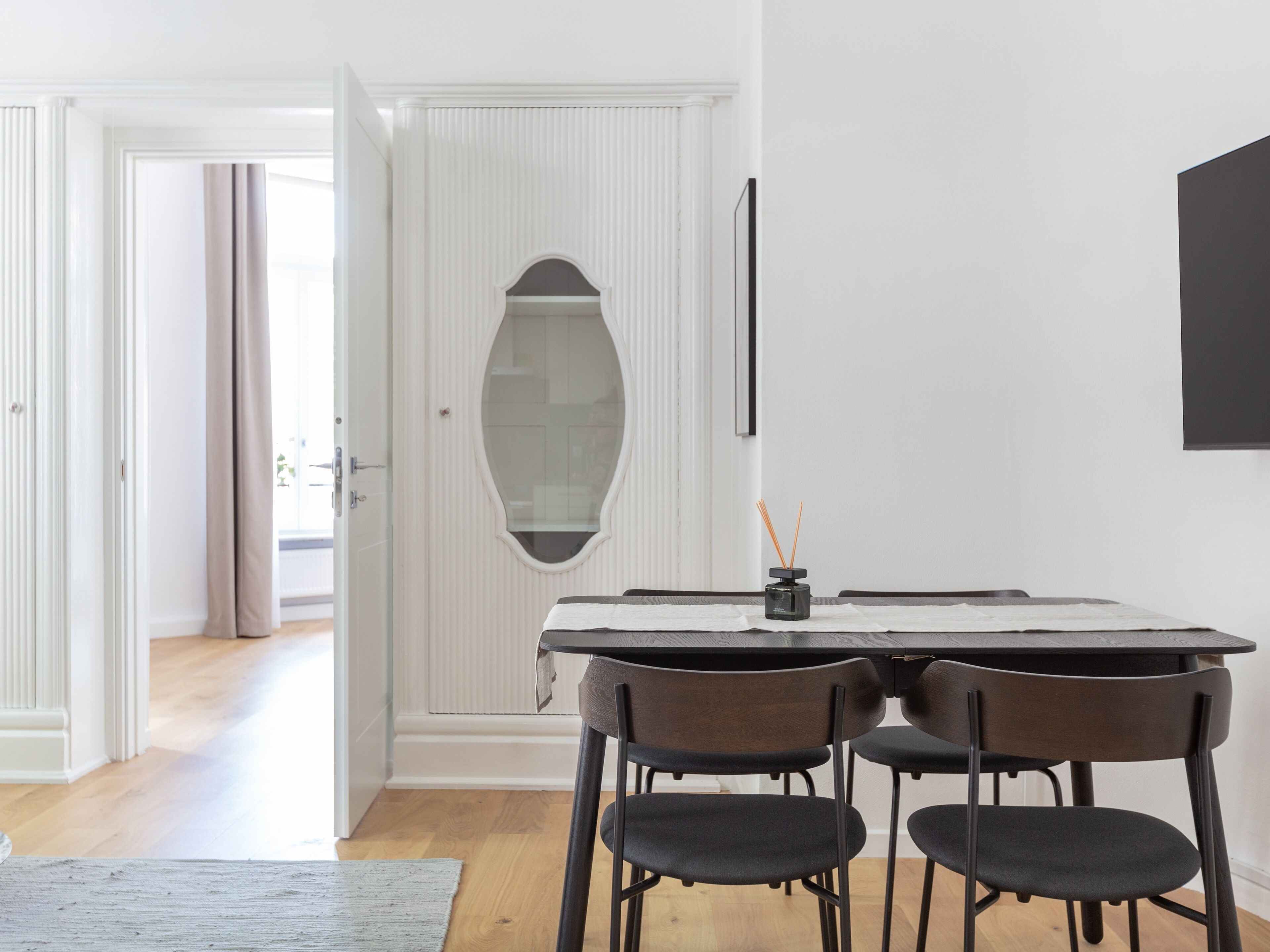 A dining area with a table, four chairs, a mirror, and a black object on the table.
