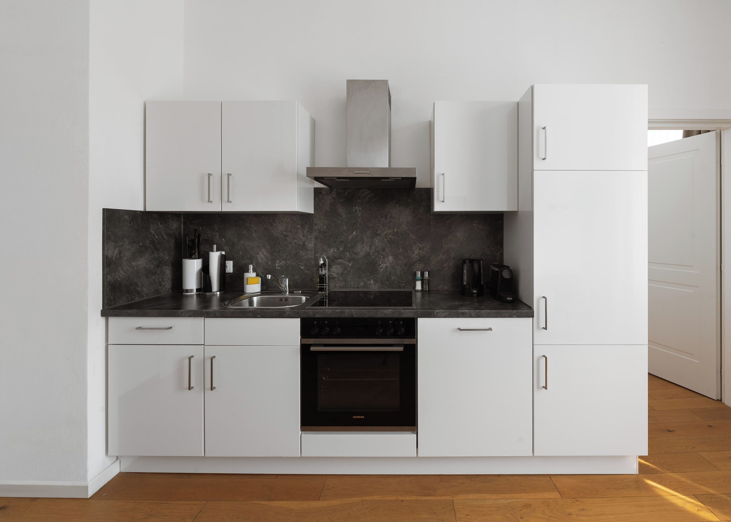 Une cuisine moderne avec des meubles blancs, un plan de travail noir, un évier en acier inoxydable et un four encastré.