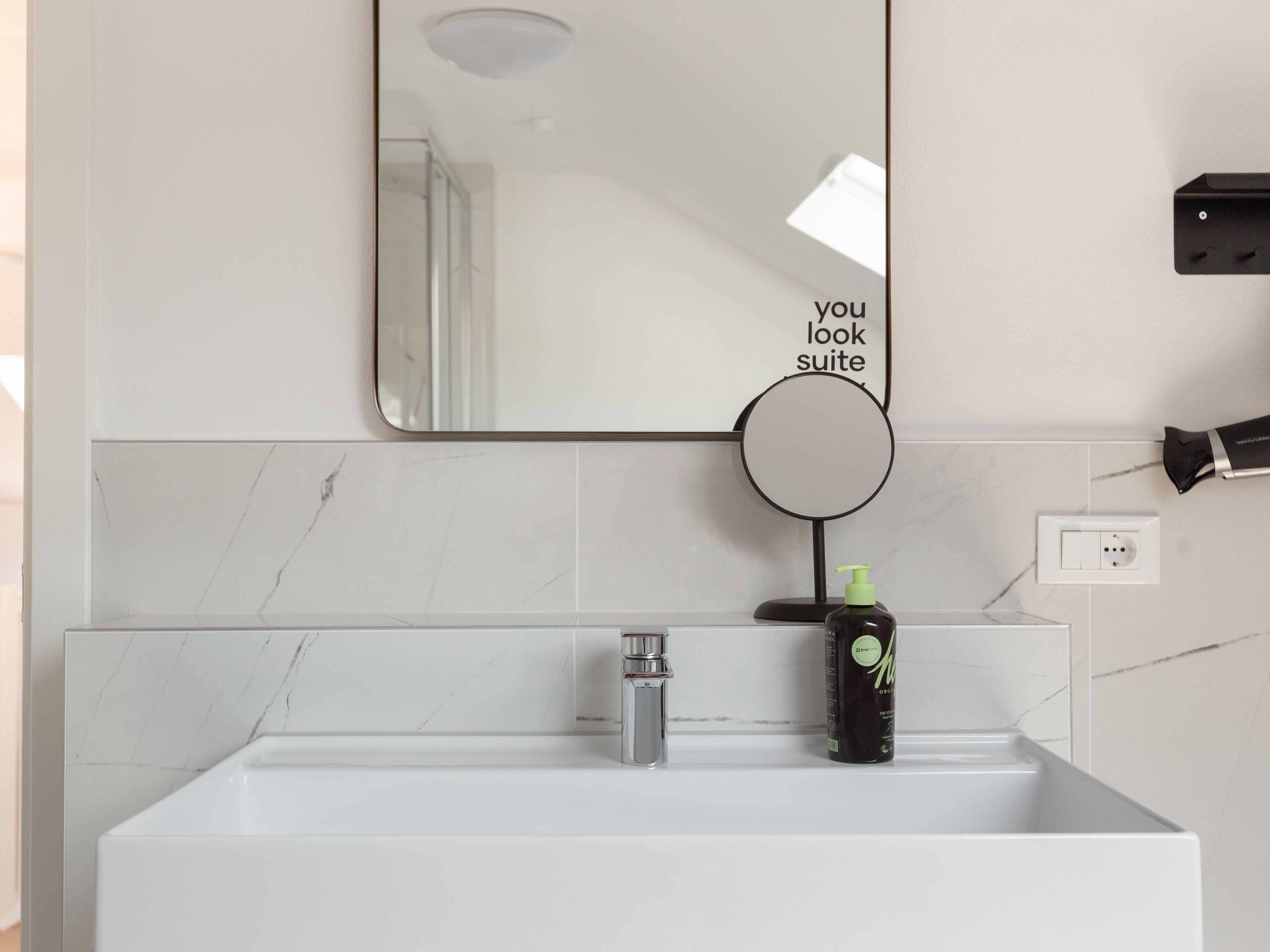 Een badkamer met een witte wastafel, een spiegel en een zeepdispenser.