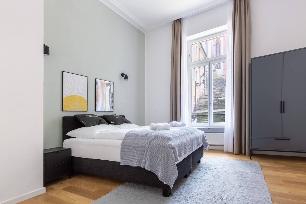 Un dormitorio con cama, mesita de noche, armario y ventana con cortinas.