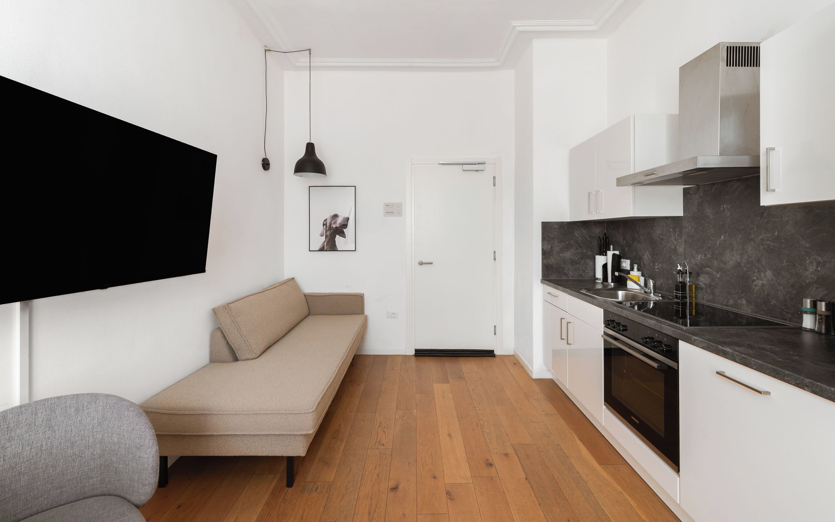 Cocina compacta con sofá, comedor y televisor negro montado en la pared.