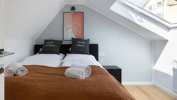 Un dormitorio moderno con tragaluces, dos camas con almohadas a juego, una manta marrón y una obra de arte enmarcada en la pared.
