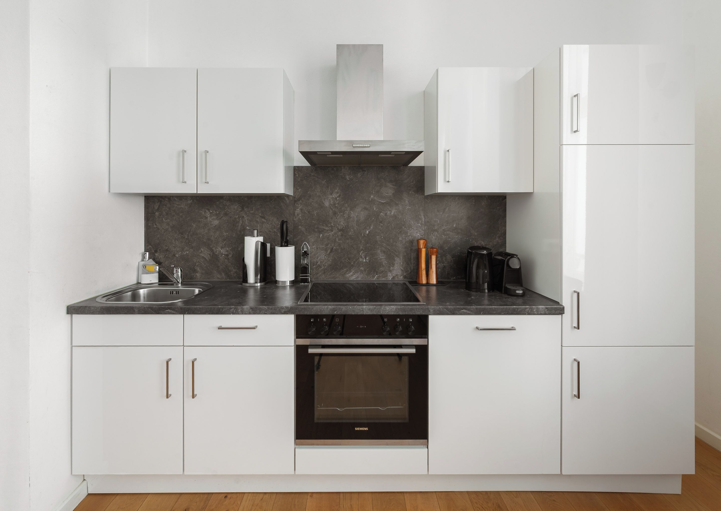A modern kitchen with white cabinets, a black countertop, and a built-in oven.