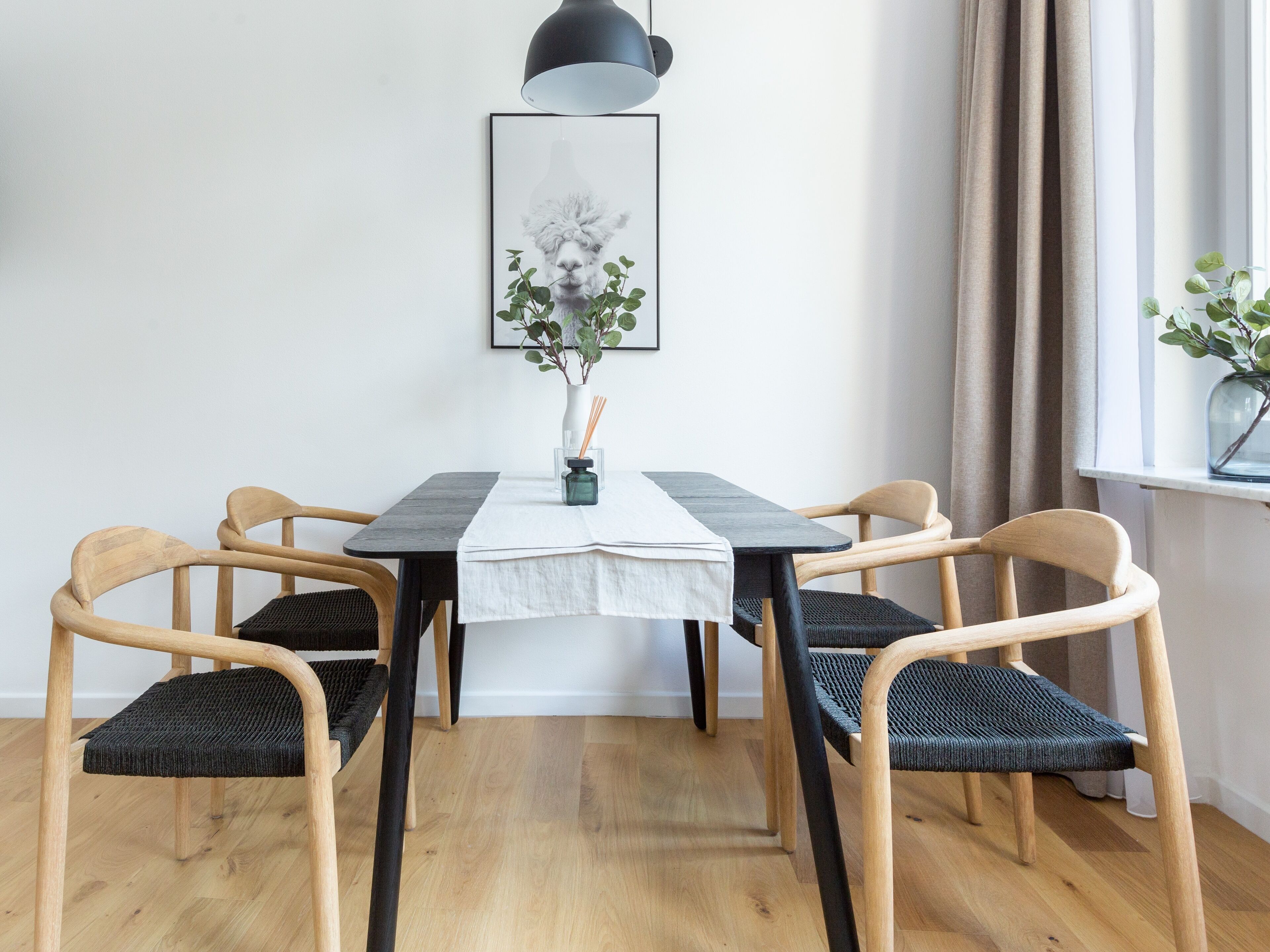 Un comedor con una mesa, sillas, un cuadro enmarcado y un ventanal con cortinas.
