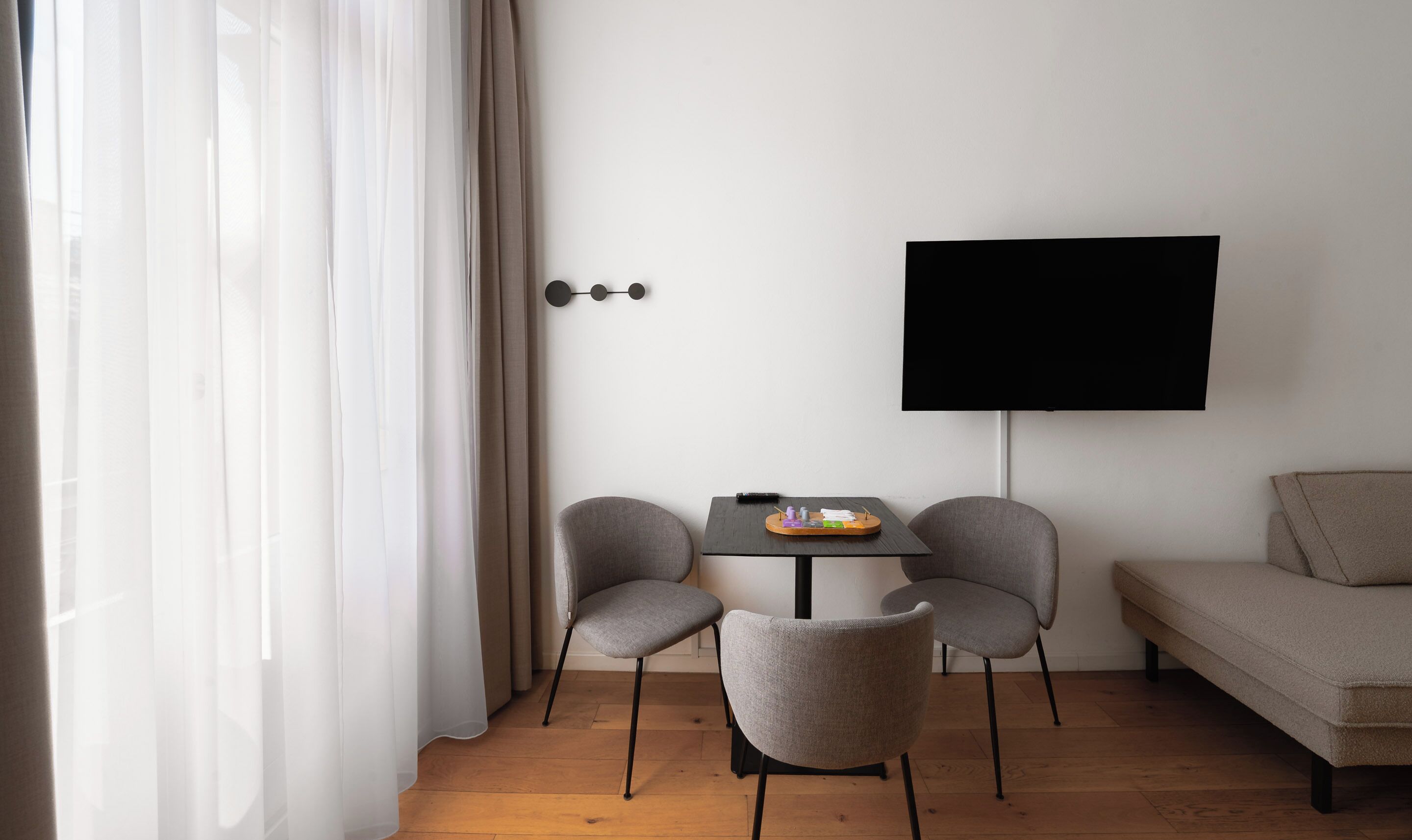 Una sala de estar moderna con un sofá, dos sillones, una mesita con una bandeja y un televisor en la pared.