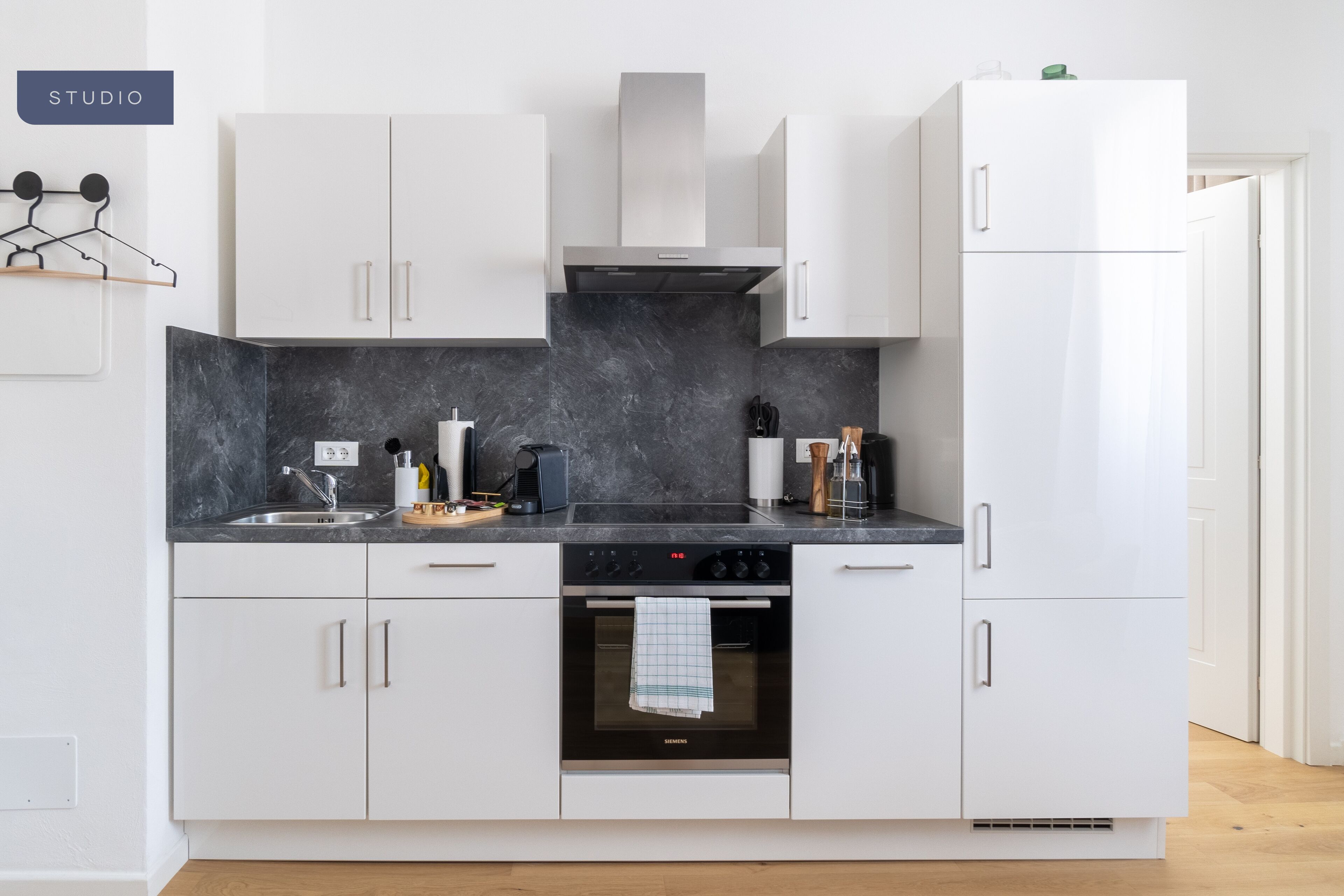 Una cocina moderna con gabinetes blancos, encimera negra y horno integrado.
