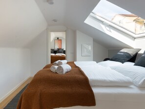 A hotel room with a skylight, a bed with white linens, a brown throw blanket, and a view of the city through the window. - Limehome Baden-Baden Bäderstraße (Baden-Baden)