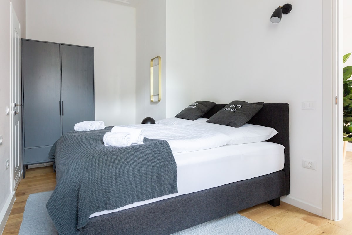 Un dormitorio moderno con una cama grande, ropa de cama gris y almohadas a juego.