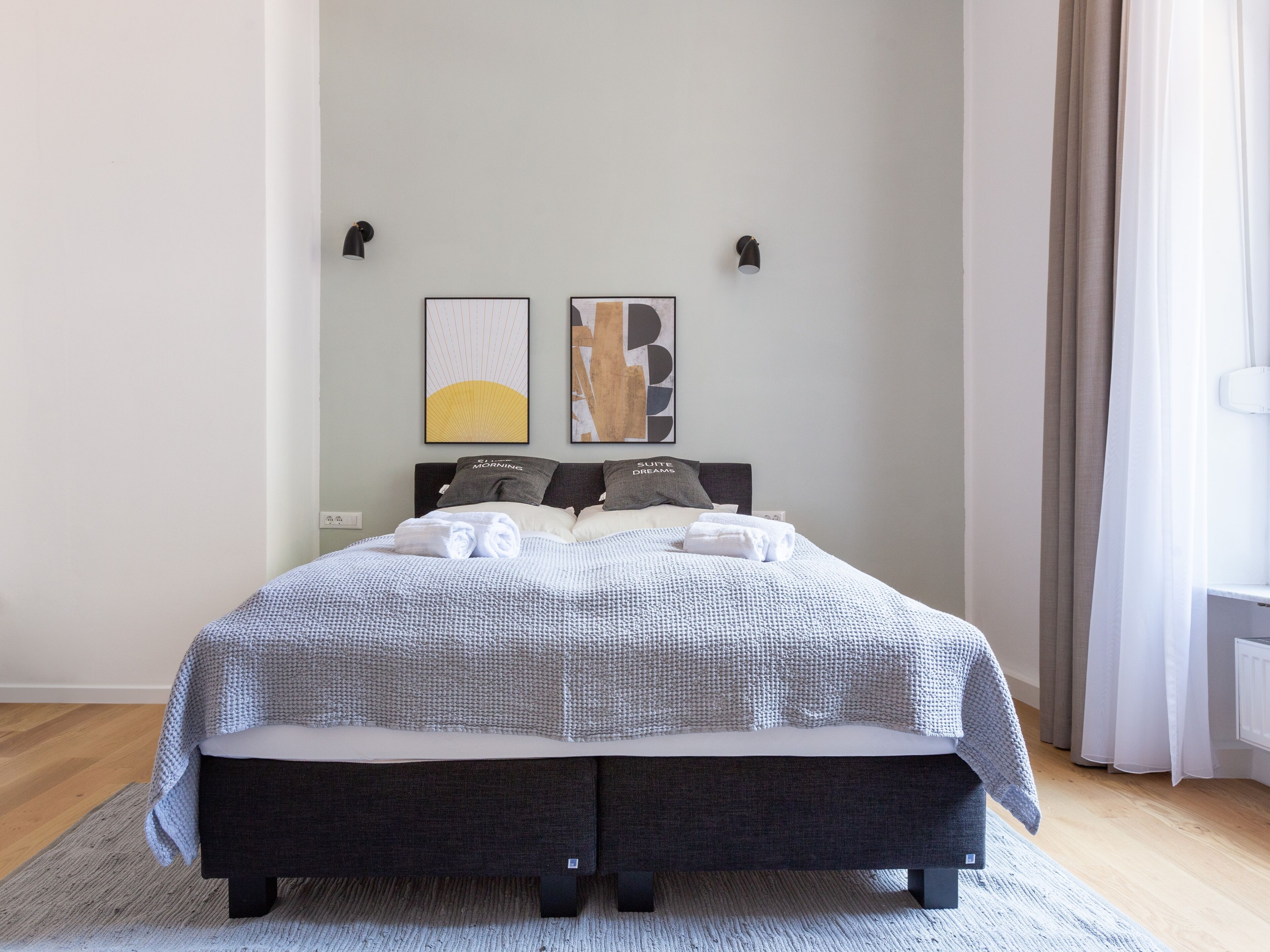Un letto rifatto con cura, coperto da un piumone a griglia grigio e bianco, due cuscini con scritte e una testiera grigia.