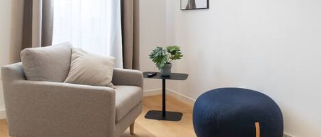 A modern living room with a grey sofa, a blue bean bag, a small table with a plant, and a framed picture on the wall.