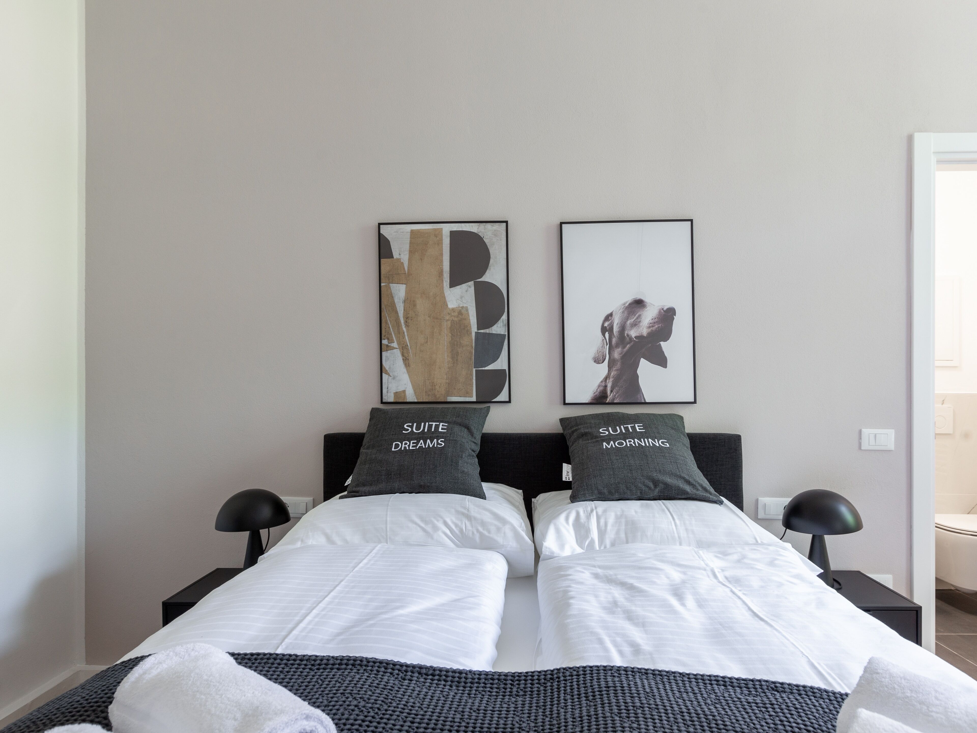 A double bed with two pillows, a bedside table with a lamp, and two framed artworks on the wall.