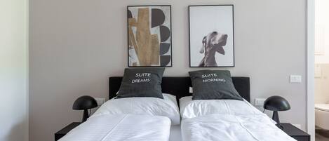 A double bed with two pillows, a bedside table with a lamp, and two framed artworks on the wall.