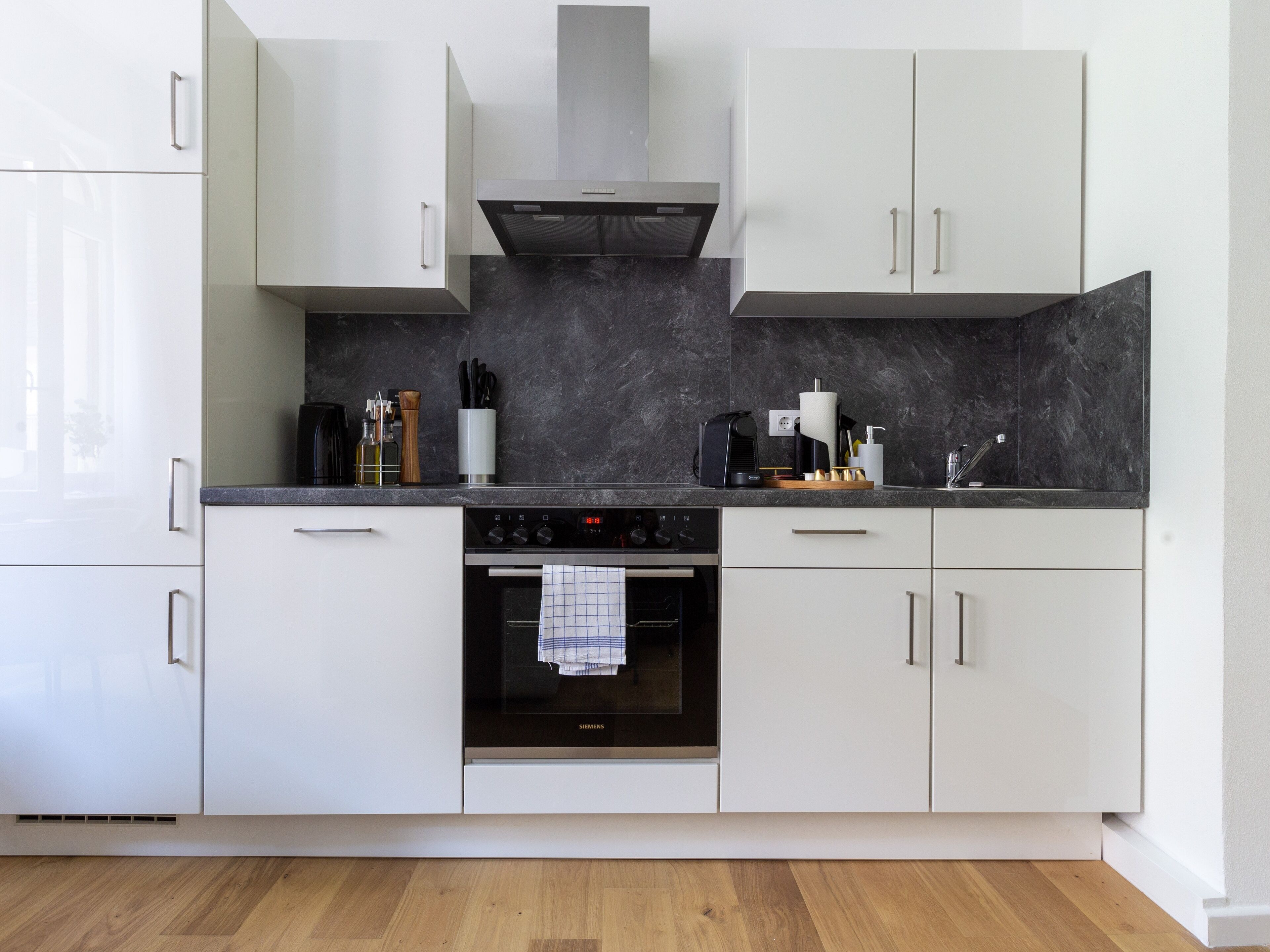 A modern kitchen with white cabinetry, a black countertop, and a Siemens oven.