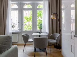 Quarto moderno com uma mesa de jantar, duas cadeiras, um abajur e janelas amplas com cortinas.