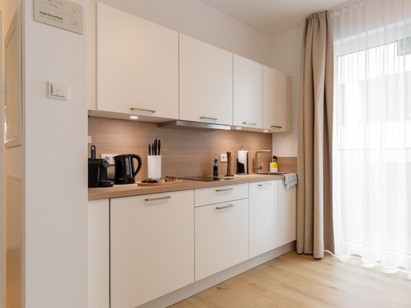 A modern kitchen with white cabinets, a wooden countertop, and a window with sheer curtains.