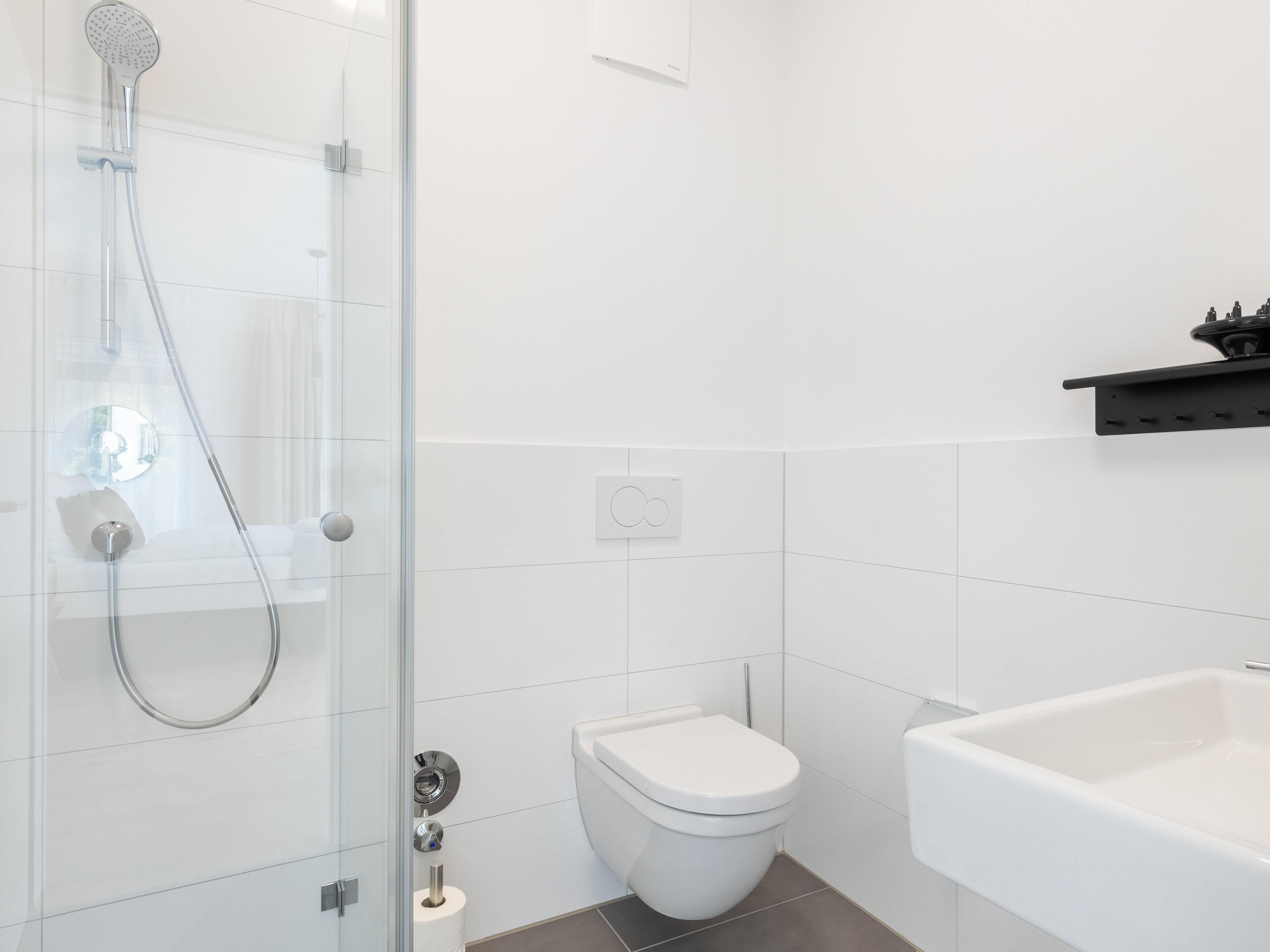 Un baño moderno con cabina de ducha acristalada, un inodoro blanco y una bañera blanca.