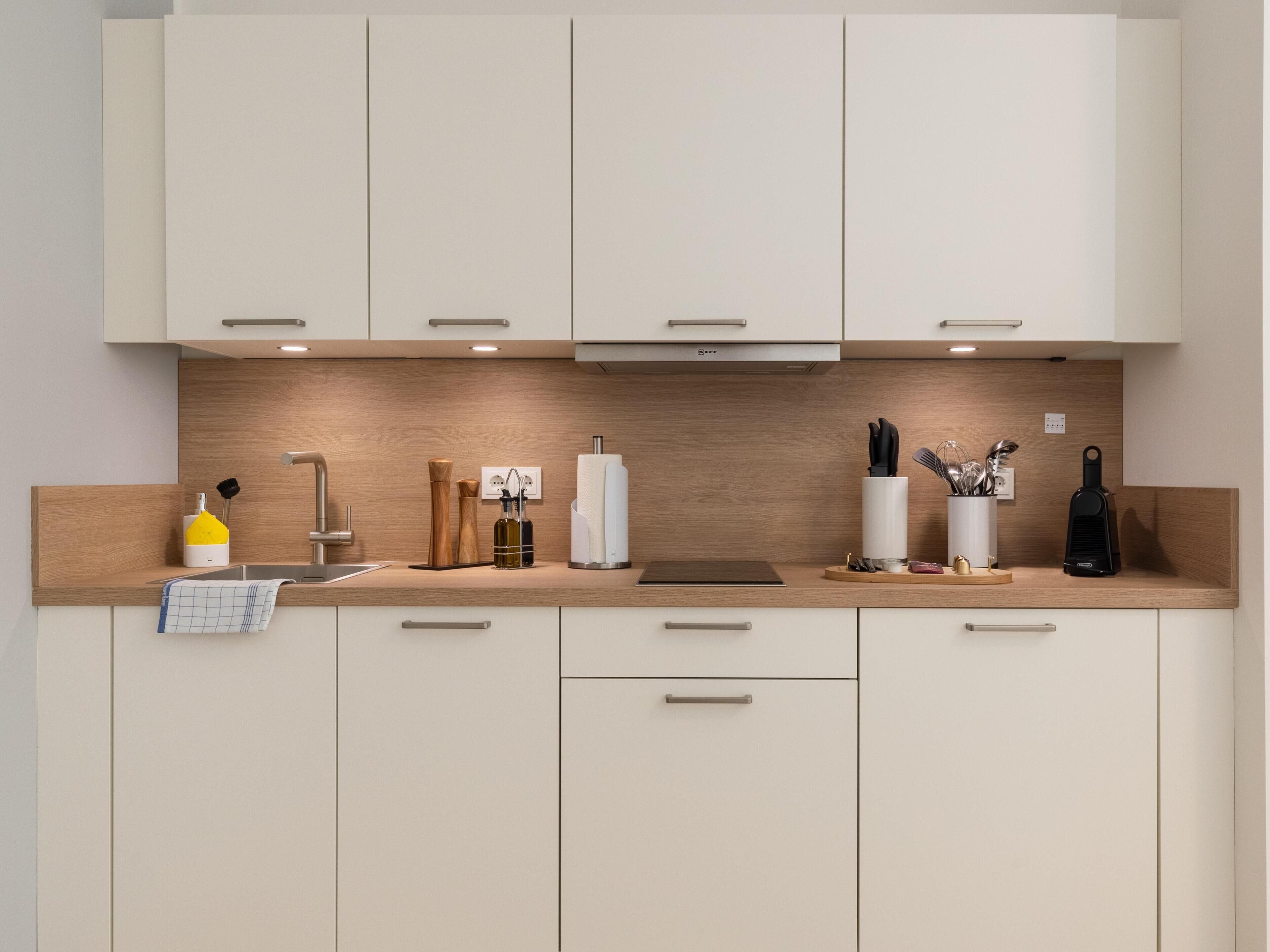Una cocina moderna con alacenas de madera clara, un lavamanos de acero inoxidable y diversos utensilios y electrodomésticos de cocina.