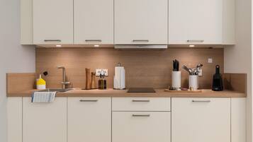 Una cocina moderna con alacenas de madera clara, un lavamanos de acero inoxidable y diversos utensilios y electrodomésticos de cocina.