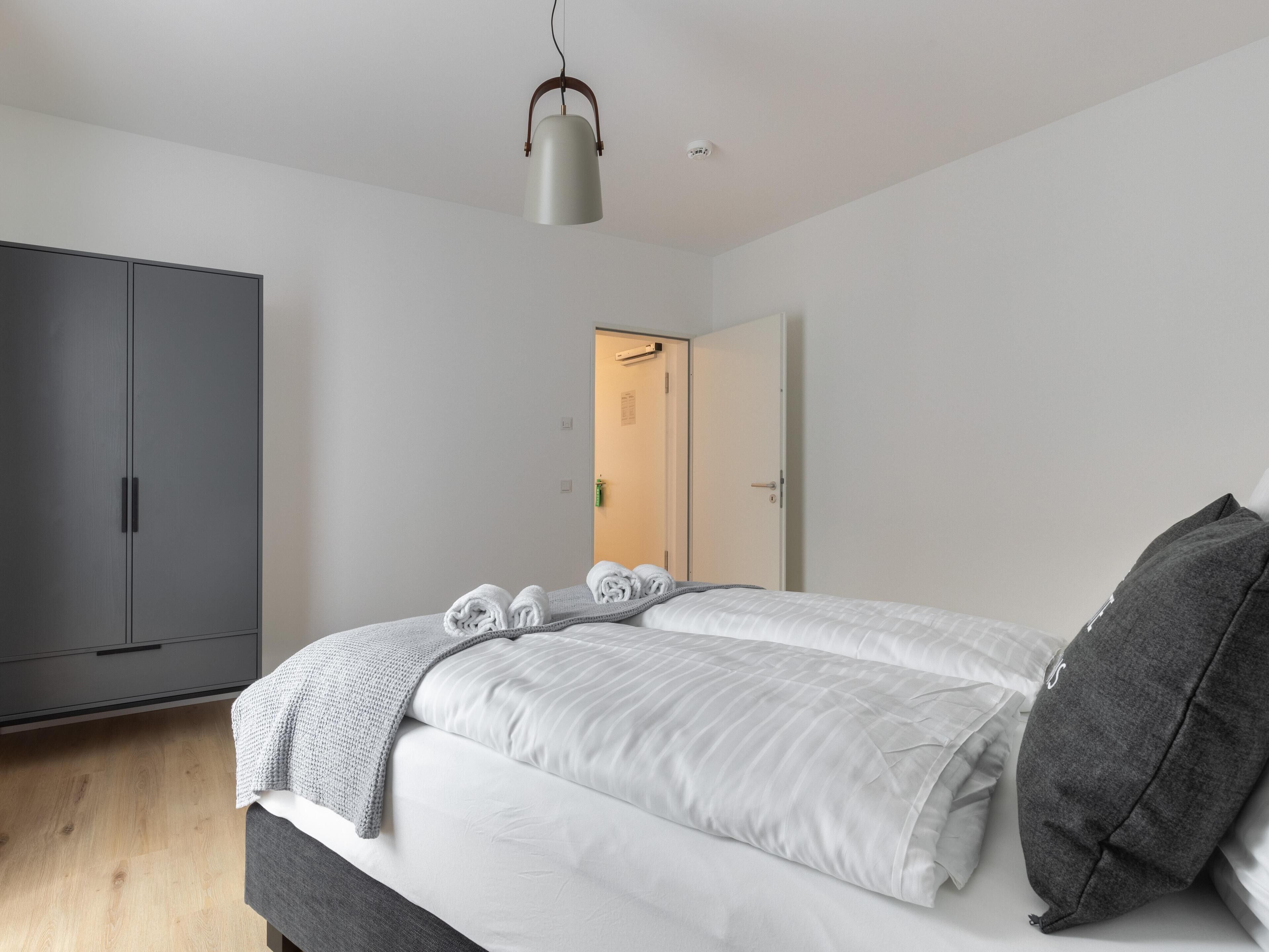 Een moderne slaapkamer met een grote kast, een bed met wit beddengoed en een grijze hoofdbord.
