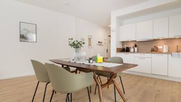 A modern dining area with a wooden table, four chairs, a vase with plants, and a framed picture on the wall.