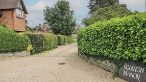 Une allée de gravier mène à une propriété appelée « Bourton Manor », avec une maison en briques sur la gauche et une haie bien entretenue sur la droite.