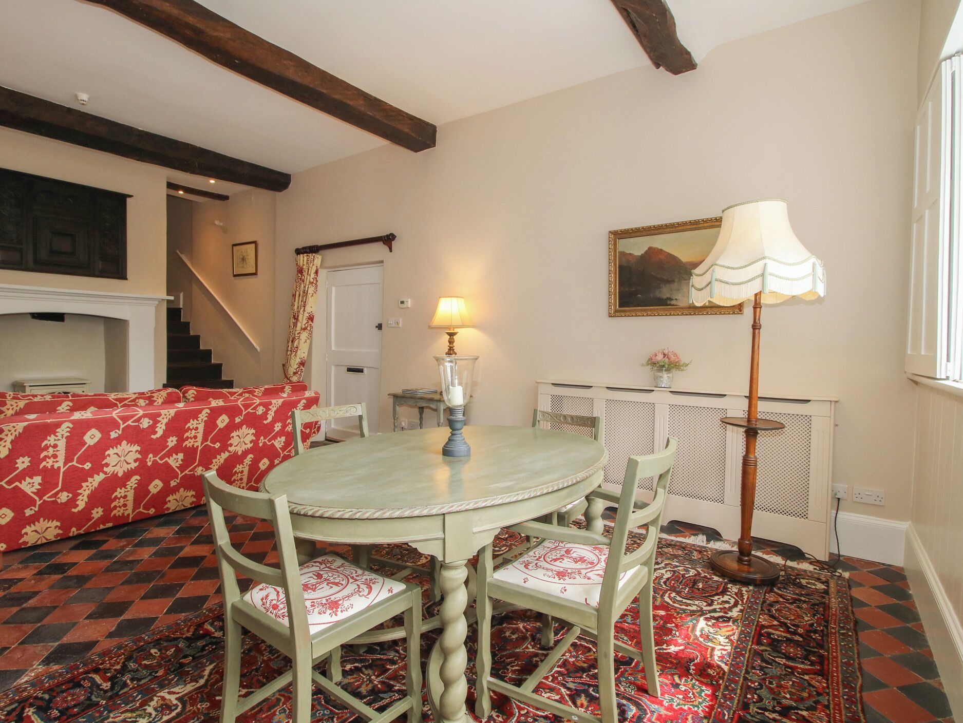 Un coin repas avec une table ronde, des chaises, une lampe, un tableau et un tapis à motifs.
