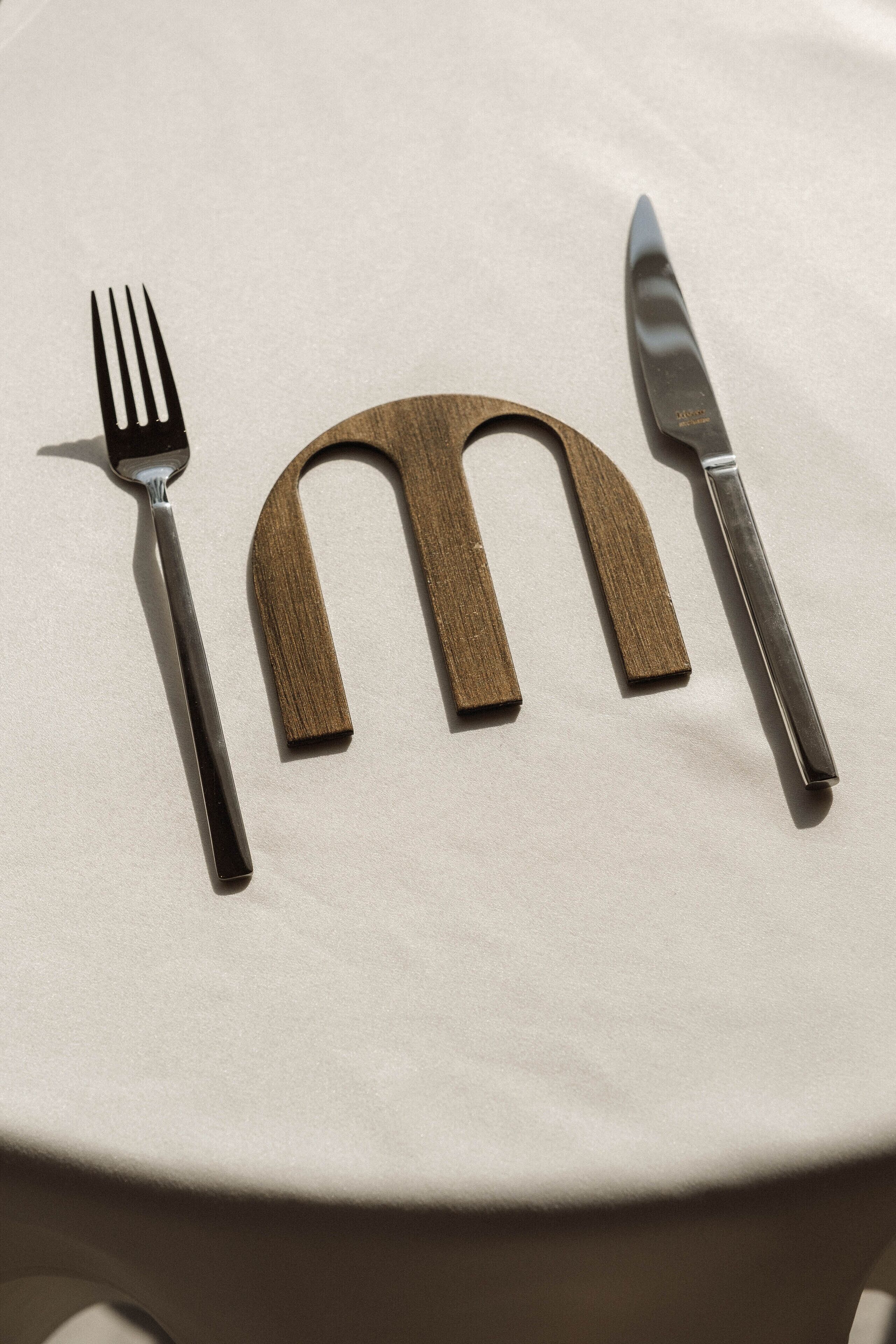 Een tafel met een vork, mes en een houten voorwerp dat op de letter 'M' lijkt.