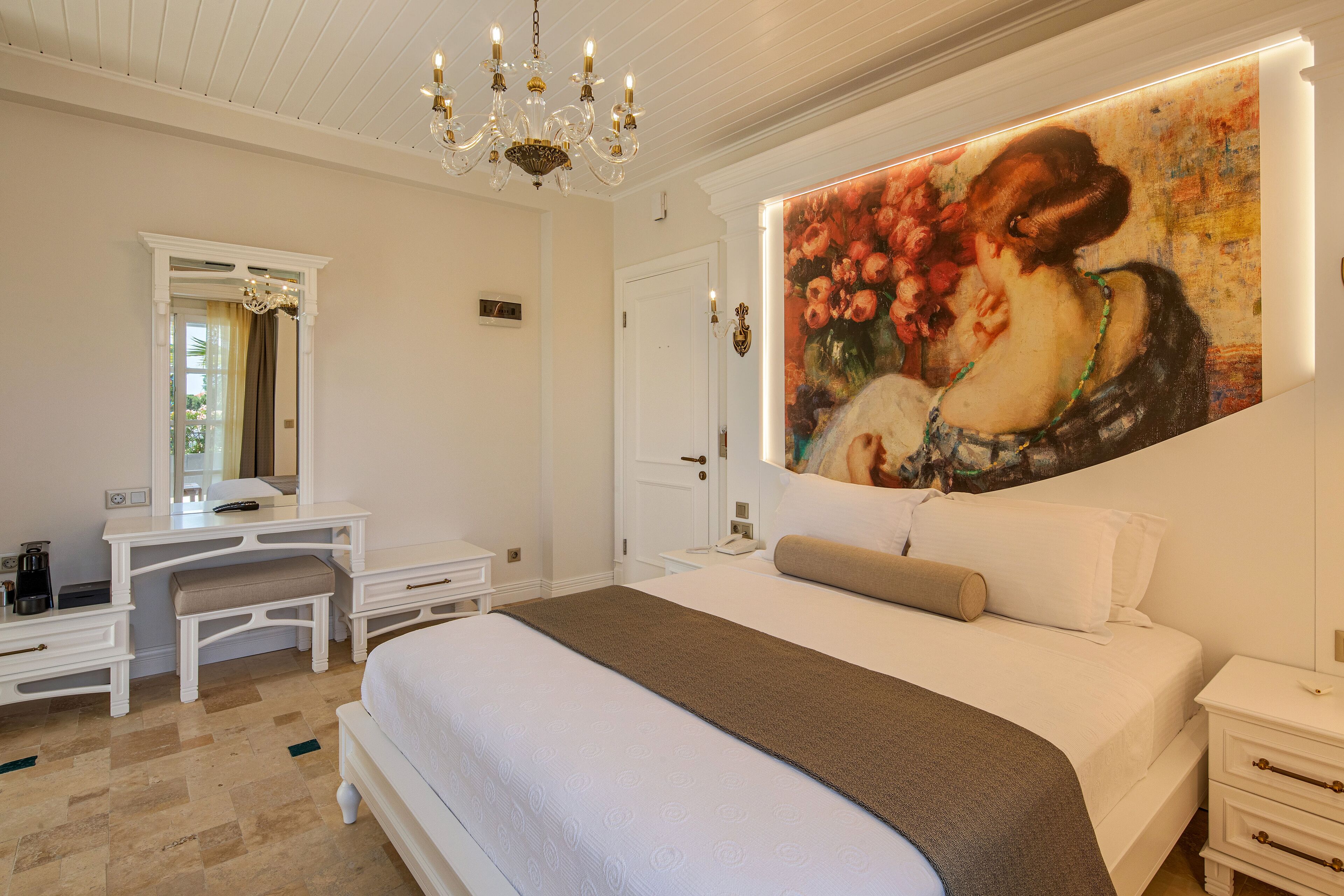 A bedroom with a large bed, a dresser, a vanity, and a painting on the wall.