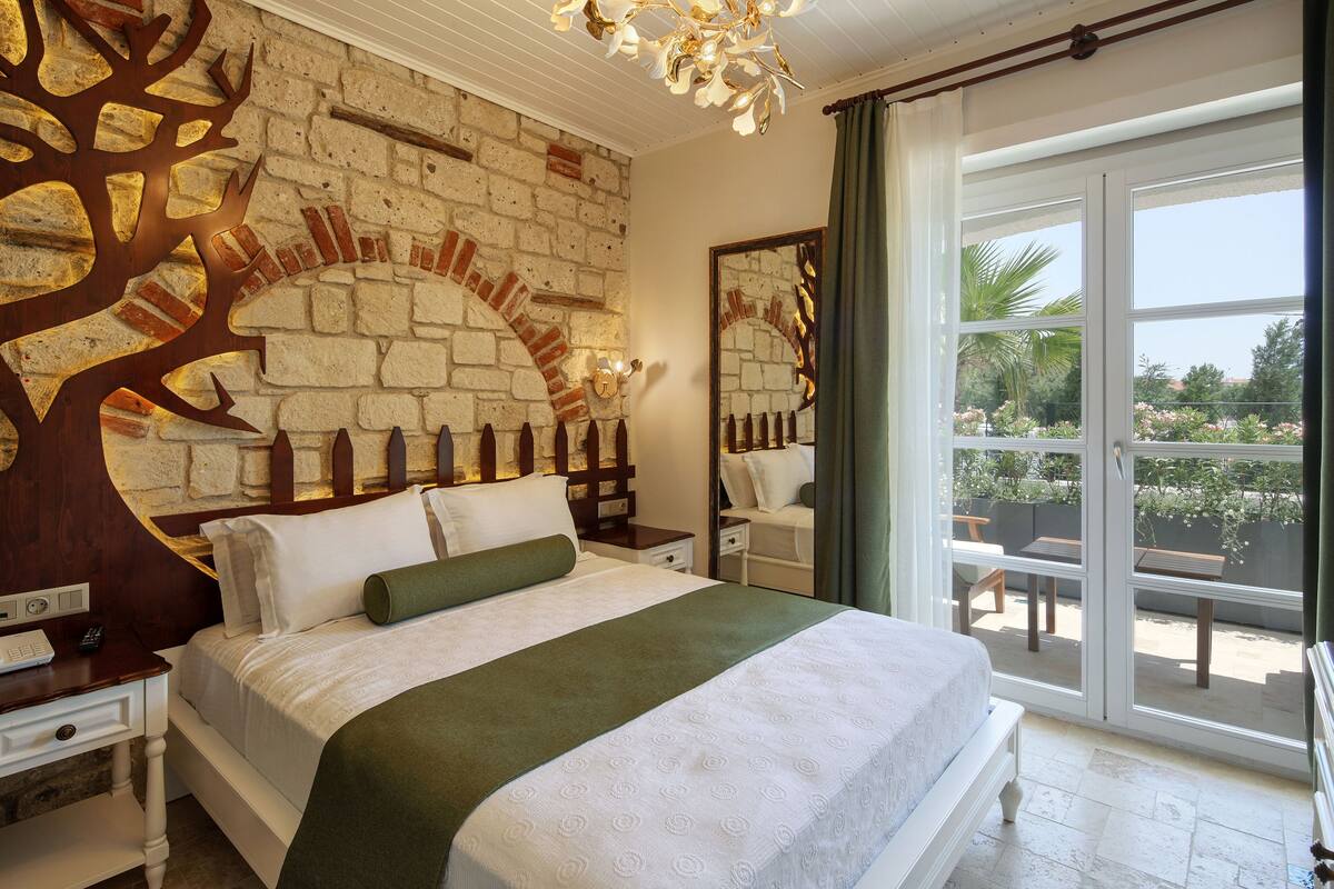 A hotel room with a brick wall, a large bed, a nightstand, a dresser, and a view of the outdoors through a sliding glass door.