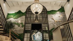 A lobby with a large chandelier, a staircase, and a wall with a green textured design. - Monreve Alaçatı (Cesme)