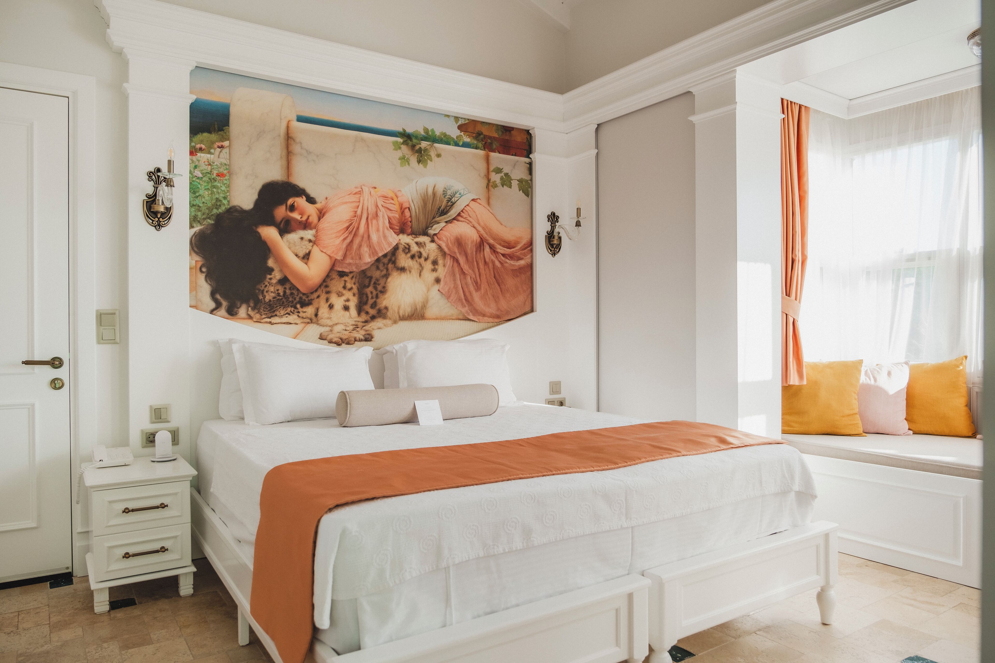 A bedroom with a large bed, a nightstand, a window with curtains, and a wall painting.