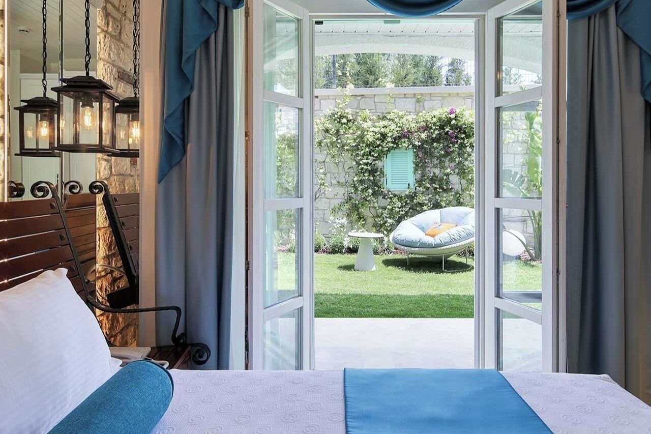 Et soveværelse med en seng, en hængende lampe og udsigt til en have gennem en glasdør.