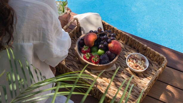 A person sitting by a poolside with a fruit basket and a drink. - Monreve Alaçatı (Cesme)