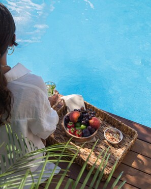 A person relaxing by a poolside with a tray of fruits and nuts. - Monreve Alaçatı (Cesme)