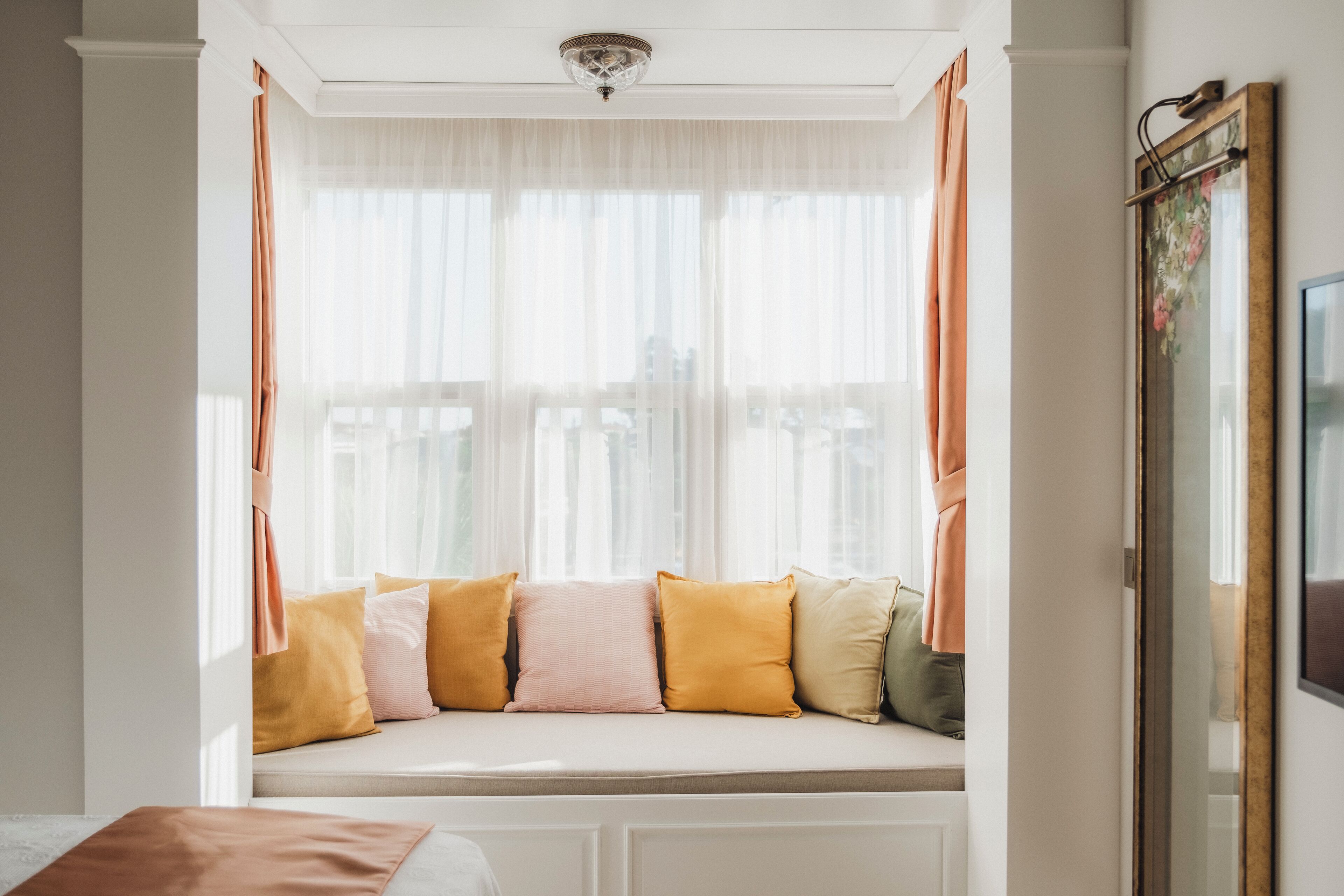 Una habitación con asiento junto a la ventana, paredes blancas y un cuadro en la pared.