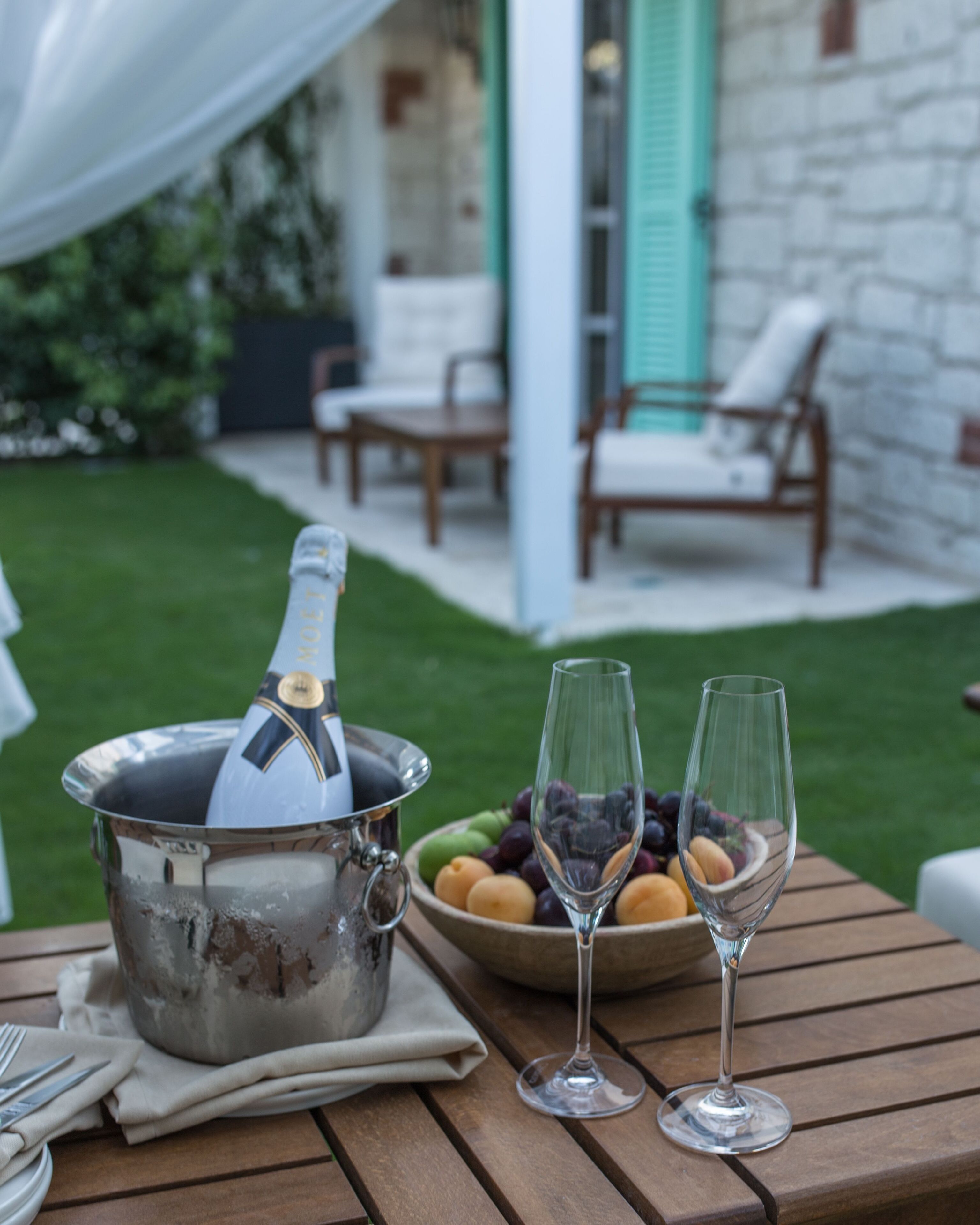 A table with a champagne bottle, two wine glasses, and a bowl of fruit.