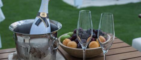 A table with a champagne bottle, two wine glasses, and a bowl of fruit.