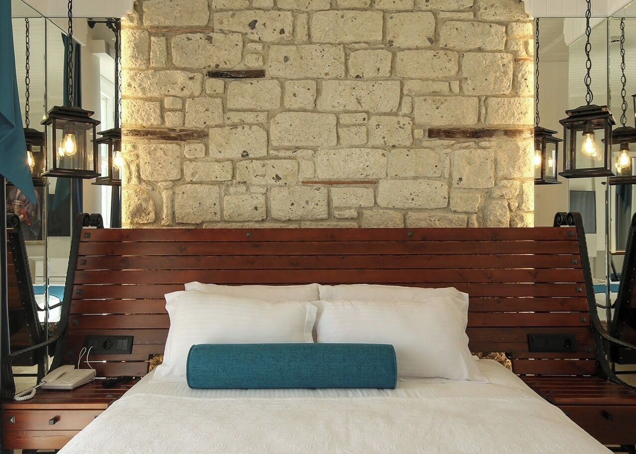 Un lit avec une tête de lit en bois, une literie blanche et un coussin décoratif de couleur turquoise.