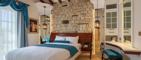 A bedroom with a stone wall, a wooden bed, a desk, and a chair.
